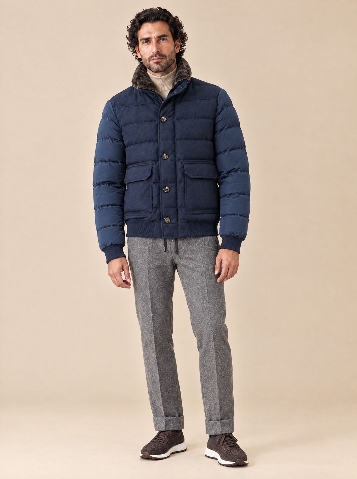 Moorer Steppjacke in Dunkelblau mit Lammfellkragen, getragen mit beigem Stehkragenpullover, grauer Kordelhose und braunen Sneakern